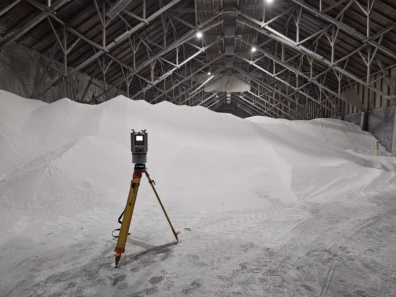 Riegl VZ-1000 terrestrial laser scanner on a tripod inside a salt warehouse, capturing a 3D scan of the bulk pile under a steel-truss roof