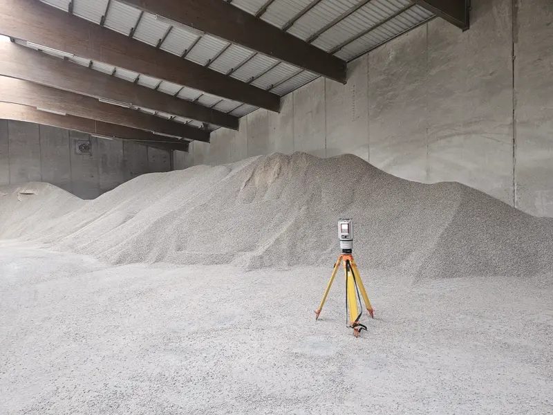 Riegl VZ-1000 terrestrial laser scanner on a yellow tripod inside a concrete-walled bulk warehouse, capturing a 3D scan of feed pellets