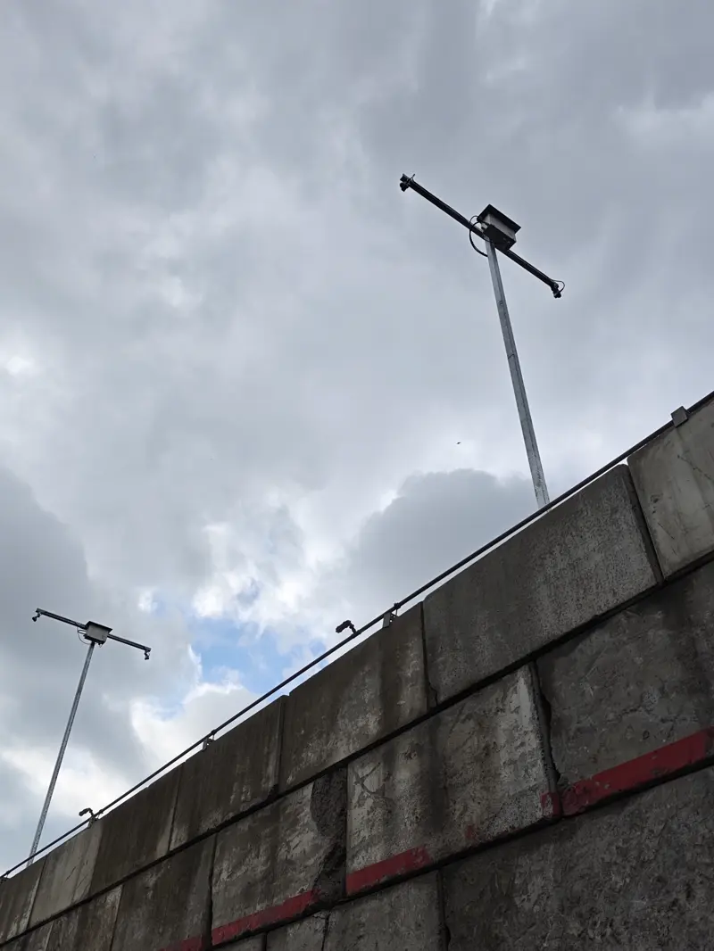 Two OWL EYE® LiDAR sensors on slim steel poles above the concrete wall of a bulk-storage bay — long-range stockpile monitoring outdoors