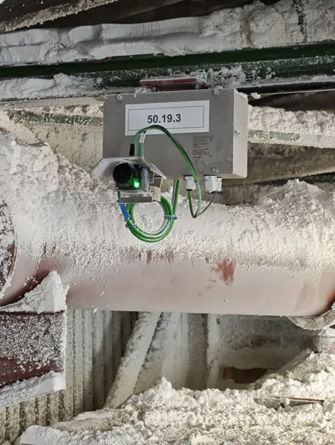 Primer plano del LiDAR 2D OWL EYE® bajo su capota protectora con el LED de estado verde encendido, en servicio entre polvo apelmazado